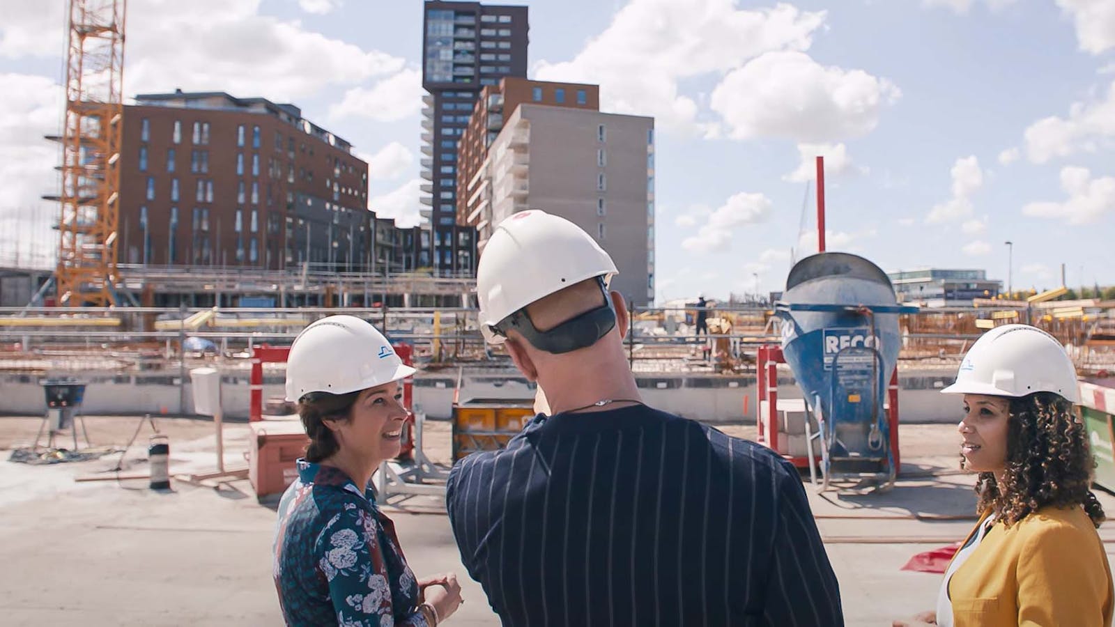 Drie mensen op een bouwplaats. Ze dragen alle drie een witte helm.