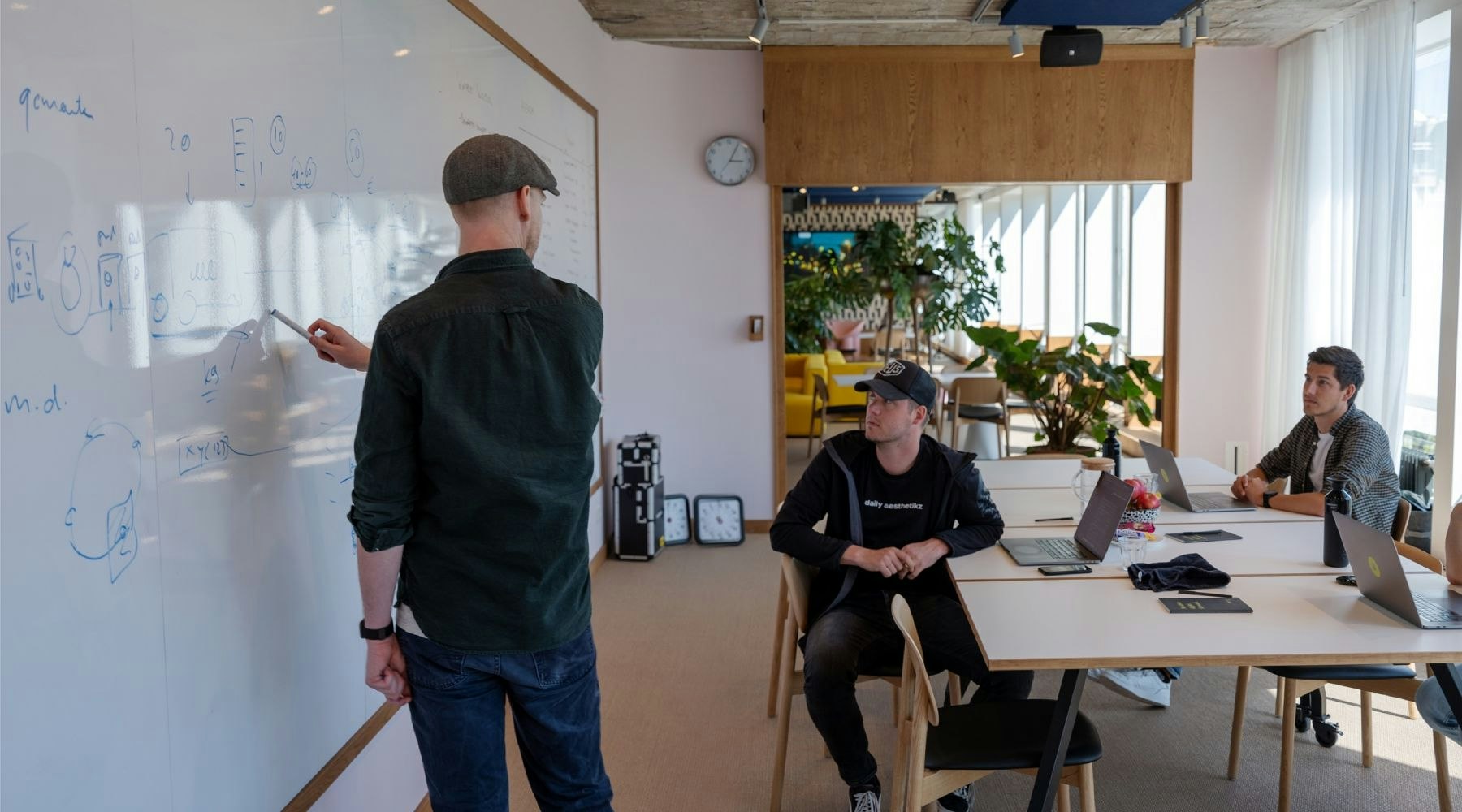 Man die iets op een whiteboard laat zien aan twee andere mannen in de ruimte.