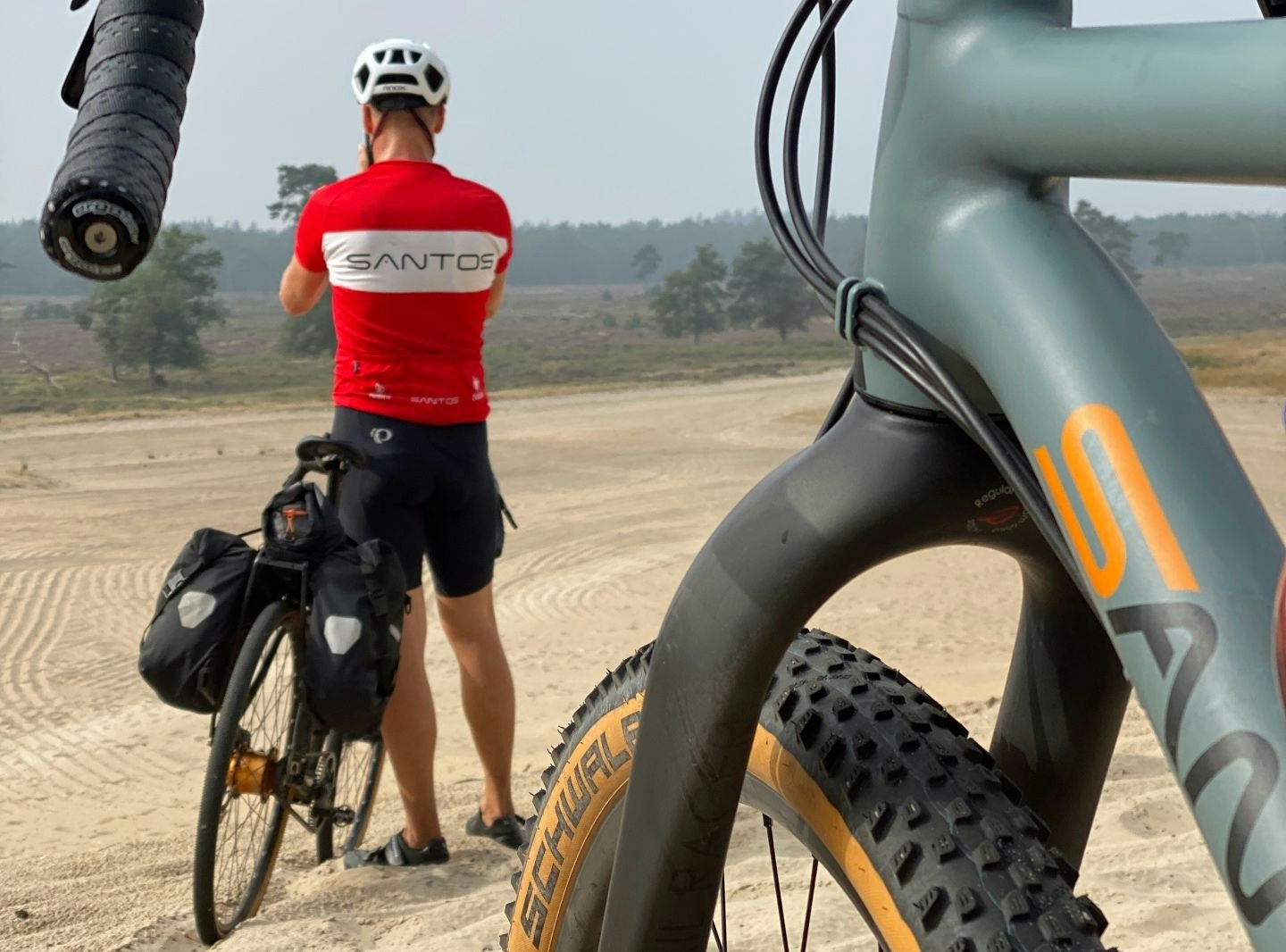 Persoon naast fiets op zanderige ondergrond.
