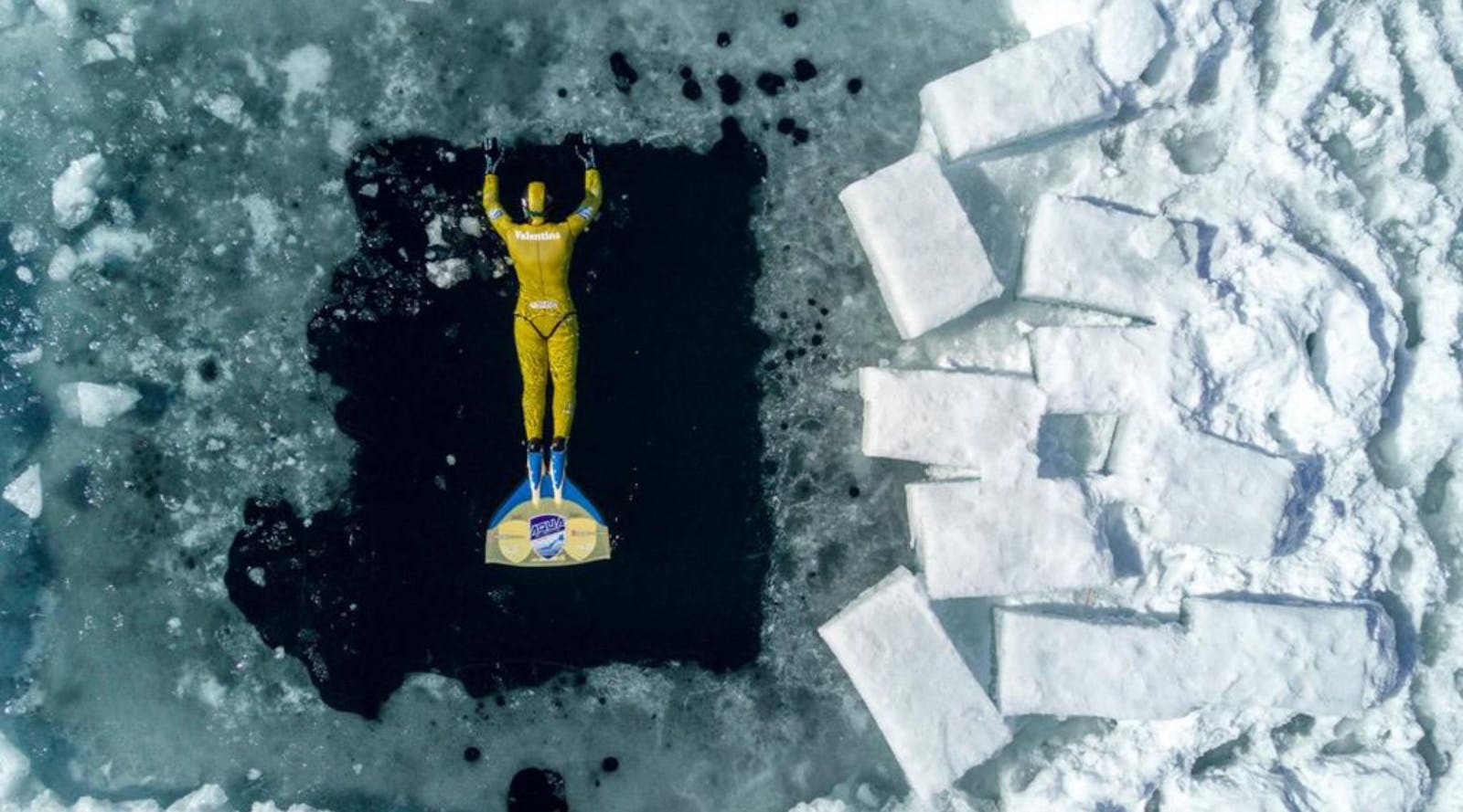 Man in geel duikpak aan het freediven in ijswater
