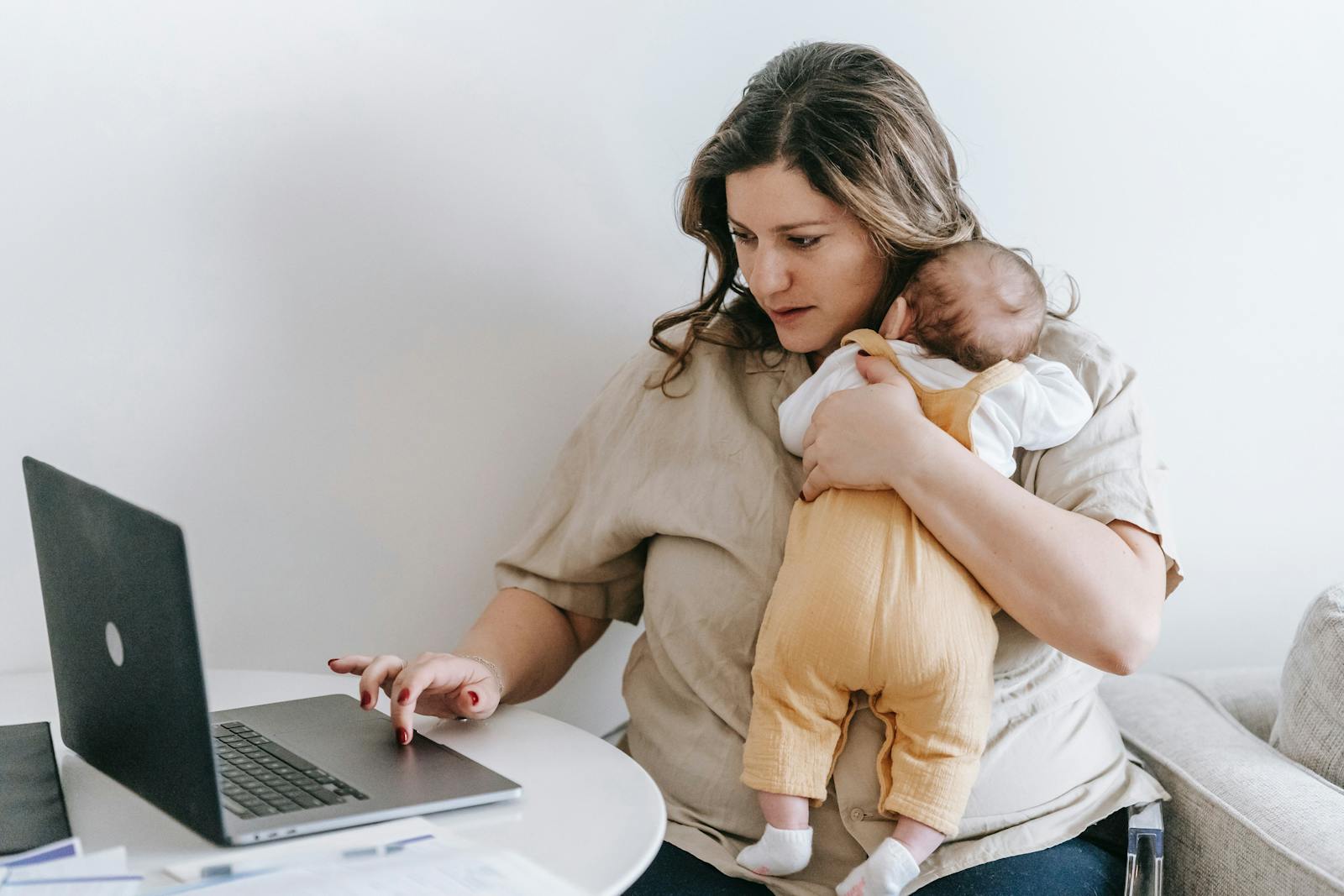 Woman with a baby who uses her laptop with one hand.